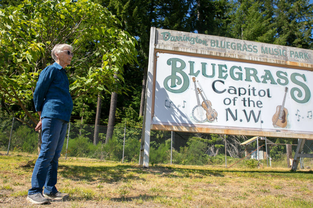 Ninety-year-old Ernestine Jones, who is one of the founders of the Darrington Bluegrass Festival, stands near the festival sign on Wednesday, at Darrington Bluegrass Music Park in Darrington. Jones planted the tree seen behind her in hopes of shading the sign and a nearby ticket booth from the sun, but it’ll be a few more decades before that hope comes to fruition. (Ryan Berry / The Herald)
