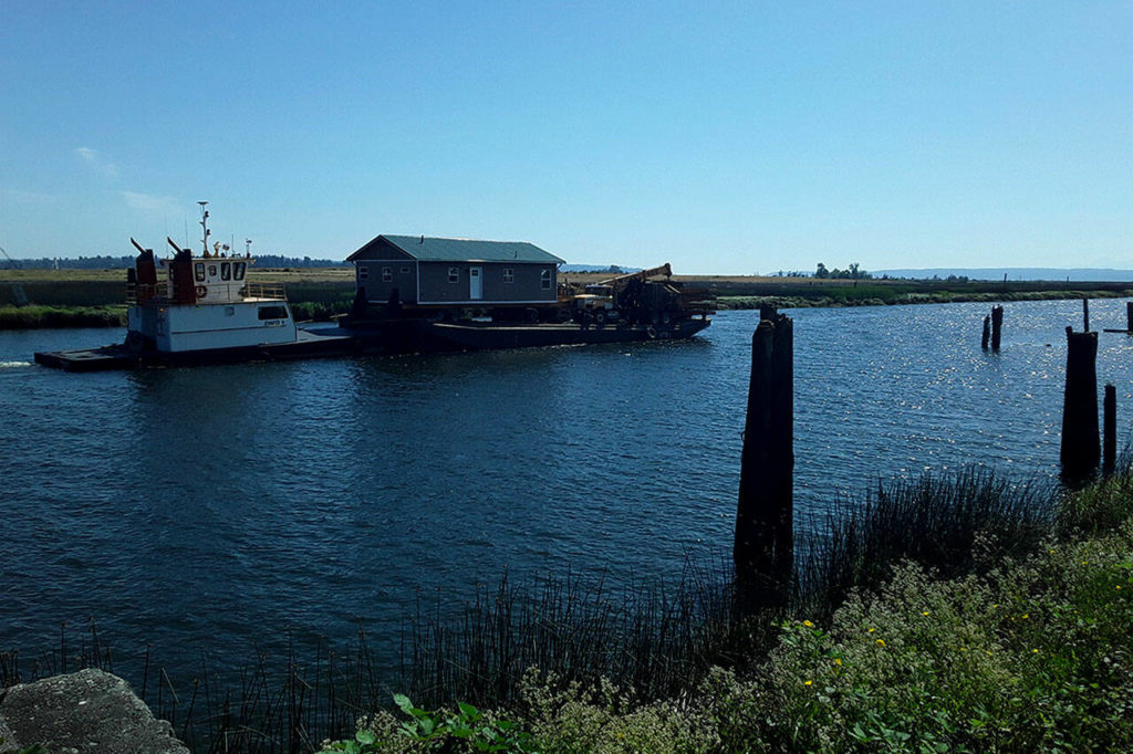 A tugboat pushes a barge carrying a home down Ebey Slough in Marysville on Thursday. (Bill Liles)
