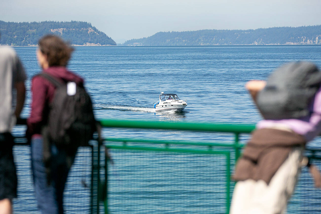 Passengers aboard the MV Suquamish ferry watch as a motorboat passes in front of the vessel as it approaches Clinton on Thursday, July 21, 2022, in the Possession Sound between Mukilteo and Clinton, Washington. (Ryan Berry / The Herald)