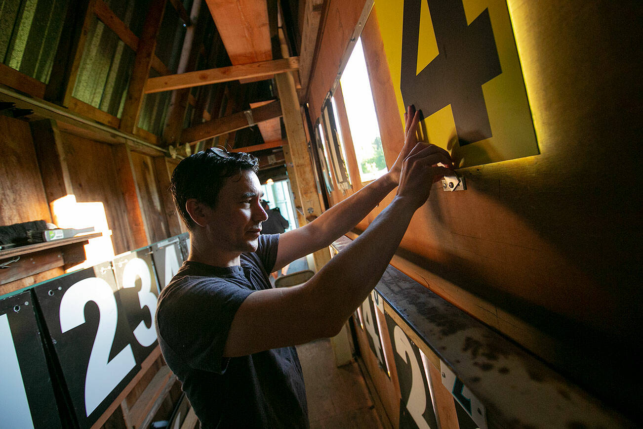 Everett Herald sports reporter Nick Patterson puts up a yellow tile to indicate runs scored in the current half inning on Saturday, July 23, 2022, inside the outfield scoreboard at Funko Field in Everett, Washington. (Ryan Berry / The Herald)
