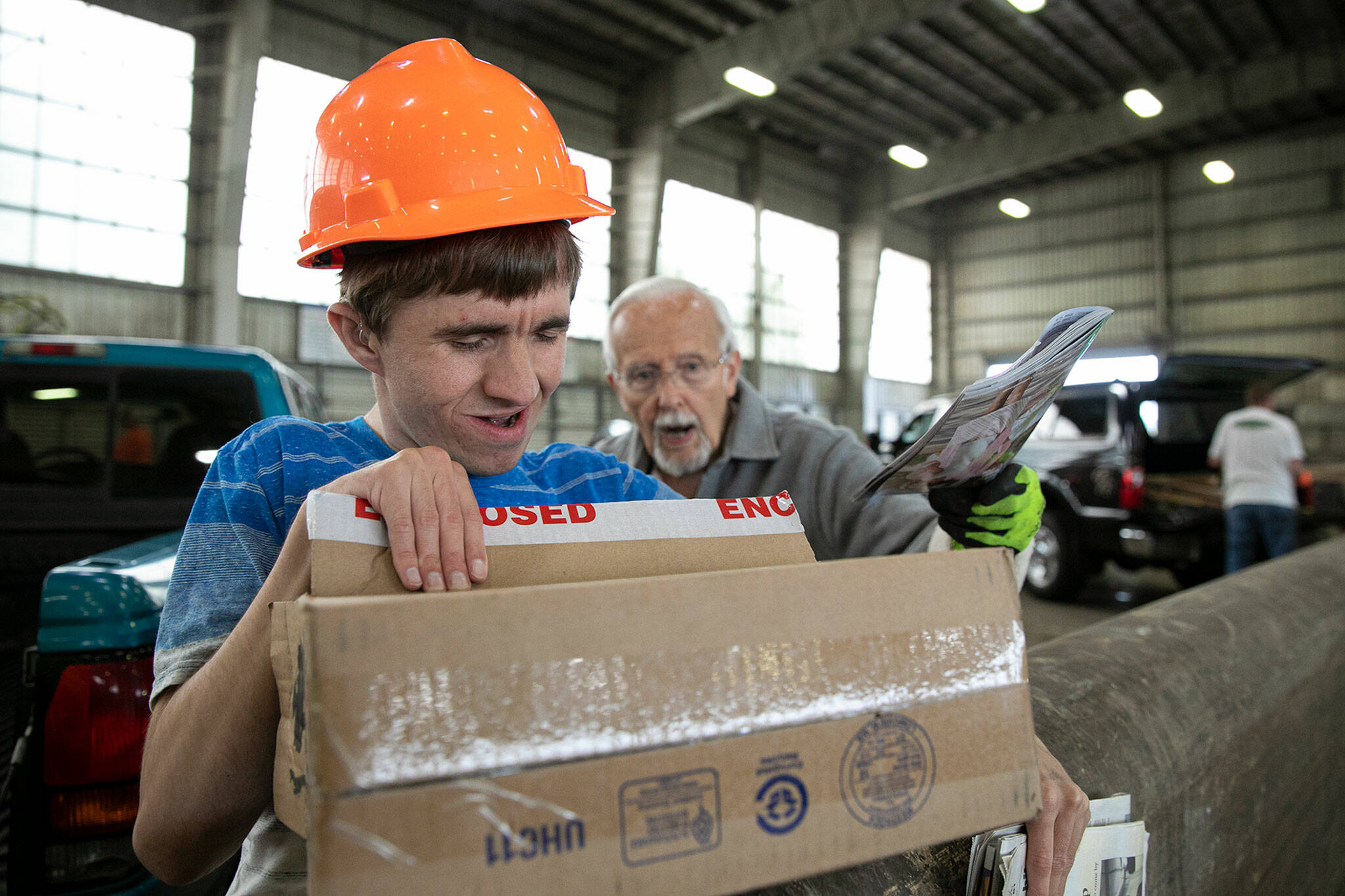 Joel Christensen, donning a hardhat gifted to him from employees at the Airport Road Recycling & Transfer Station in Everett, tosses old newspapers with the guidance of his grandfather, Harold Christensen. (Ryan Berry / The Herald)