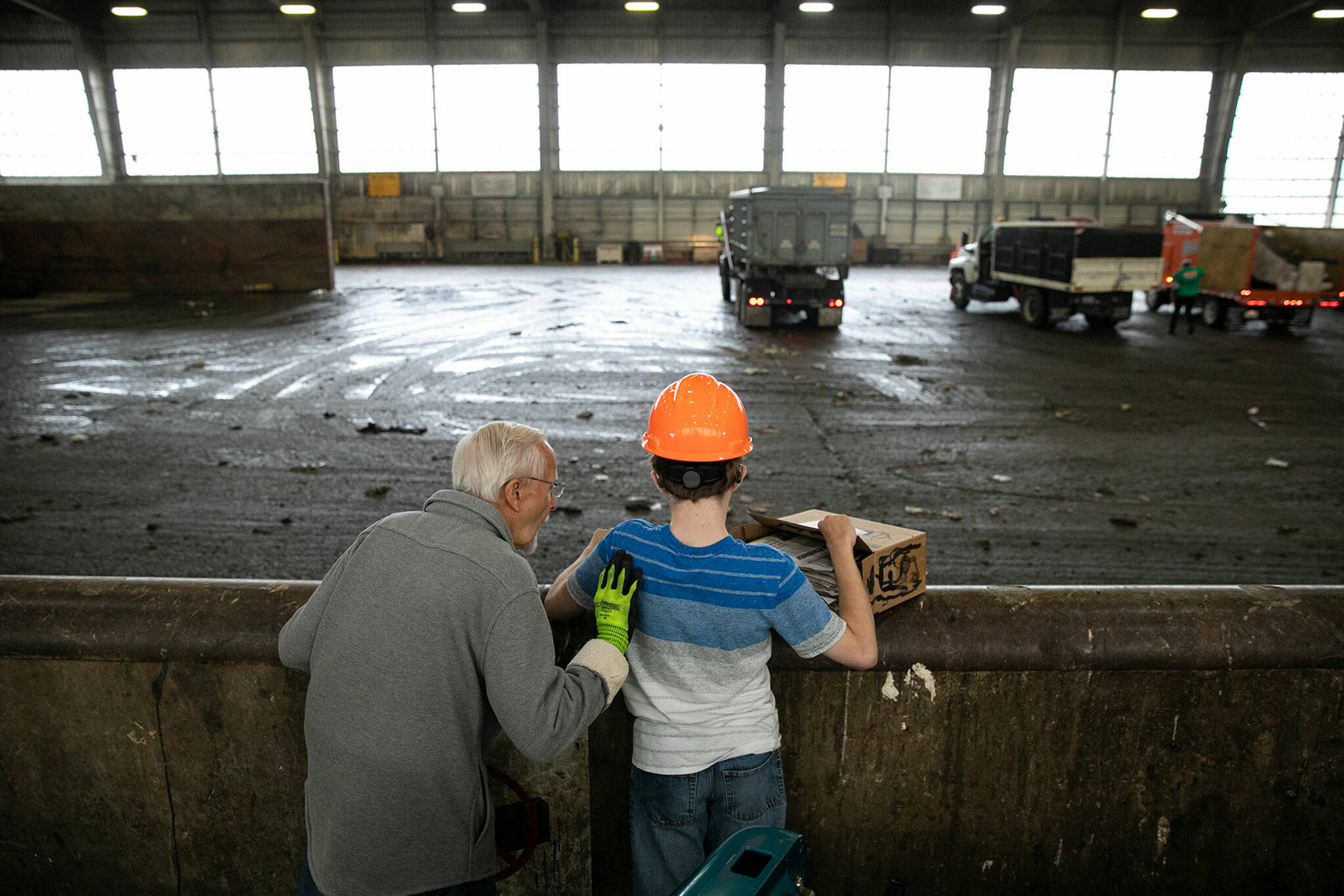 Joel Christensen, who was born with Infantile Refsum disease, causing him to be unable to see or fully hear, stands with his grandfather Harold at his side as he tosses trash into the pit at the Airport Road Recycling & Transfer Station in Everett. Going to the transfer station is one of Joel’s favorite activities with the vibration of humming machinery, the whooshing of front-end loaders and the tactile nature of his family’s trash all stimulating his strongest senses. (Ryan Berry / The Herald)