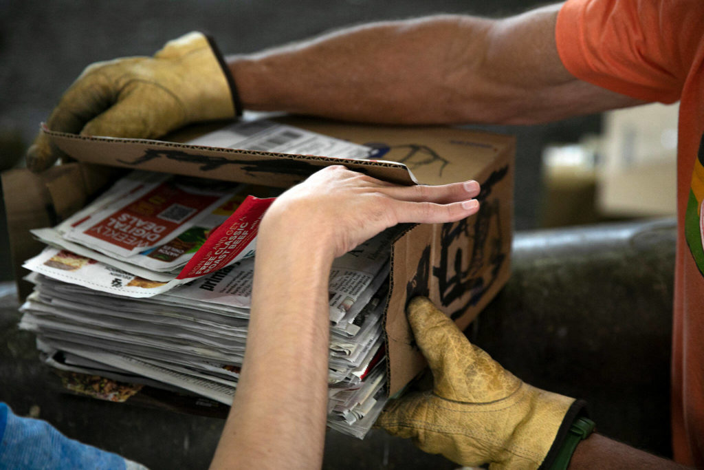 Craig Christensen holds a box of old newspapers so his son, Joel, can grab papers and throw them into the pit at the Airport Road Recycling & Transfer Station in Everett. (Ryan Berry / The Herald)
