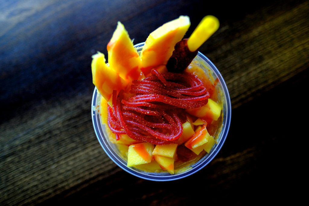 The mangonada at Las Fridas in Everett is the perfect sweet-spicy combo. The Mexican snack has mango shaved ice mixed with chamoy and tajin, and is topped with fresh mango, watermelon salsagheti candy and a tamarind stick. (Taylor Goebel / The Herald)
