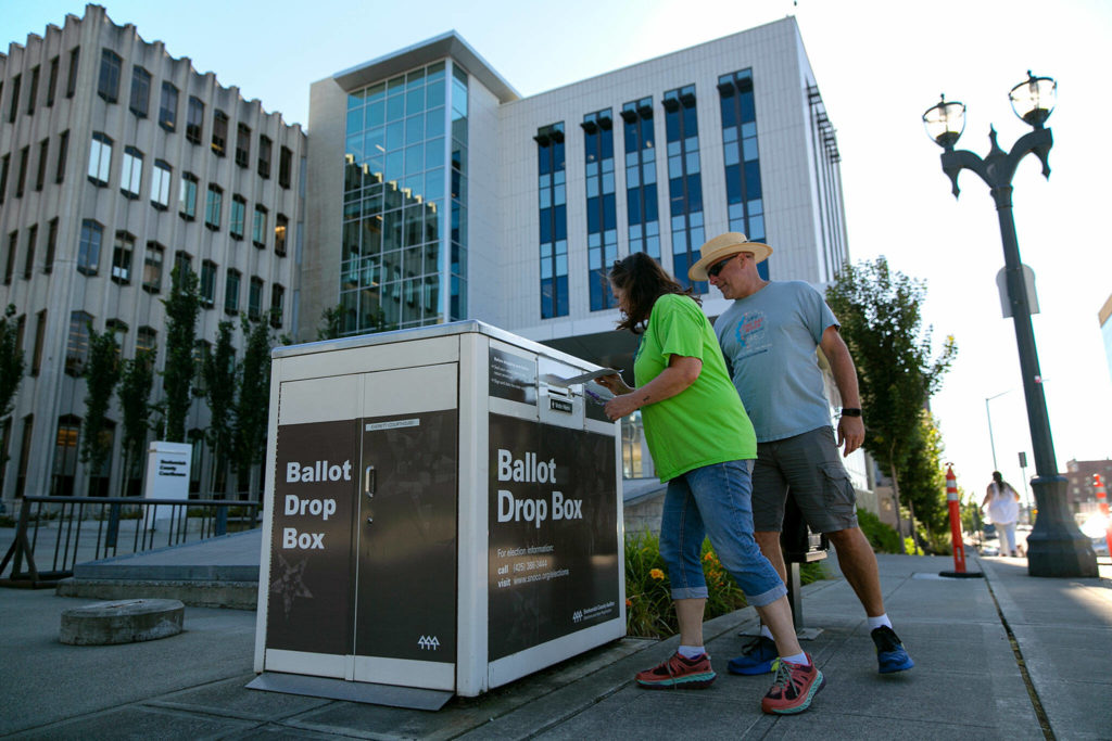Everett residents Arlene and Al Davis drop off their midterm primary ballots as a steady stream of voters come and go Tuesday, Aug. 2, 2022, at the drop box in front of the Snohomish County Courthouse in Everett, Washington. “We’re happy to do this,” Arlene said. “We even walked from our house to save some gas.” (Ryan Berry / The Herald)
