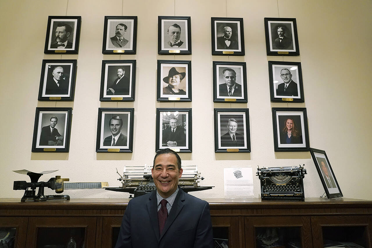 Steve Hobbs, who was sworn in as Washington Secretary of State, Nov. 22, 2021, at the Capitol in Olympia, poses in front of photos of the 15 people who previously held his office. (AP Photo / Ted S. Warren)