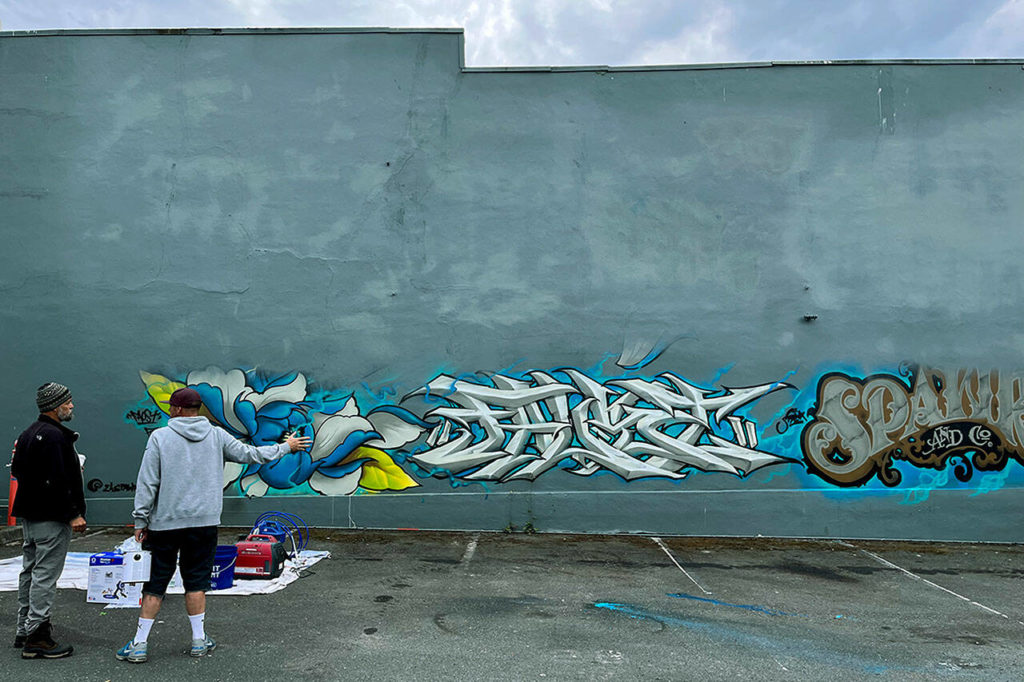 Graffiti artists on Tuesday paint over a mural created during the “Going All City NW” event on Rucker Ave. in Everett. (Jacqueline Allison / The Herald) 
