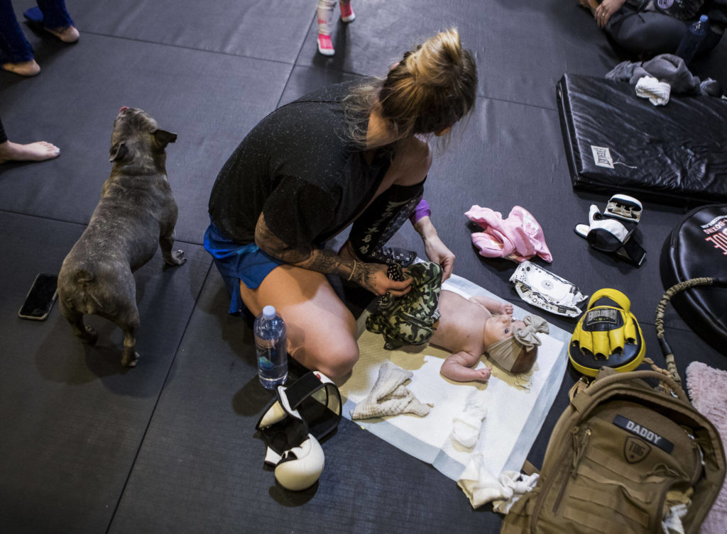 Before a workout class, Miranda Granger changes her daughter’s diaper on the floor of Charlie’s Combat Club on Nov. 8, 2021, in Everett, Washington. Granger often brought Austin with her to the gym, along with a baby bag of items for diaper changes, toys, blankets and snacks. (Olivia Vanni / The Herald)
