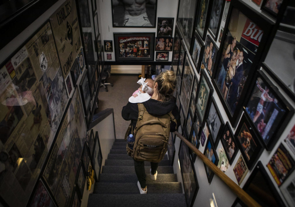 Miranda Granger holds Austin and walks down a hallway covered in photographs of fighters at Charlie’s Combat Club on Monday, Nov. 8, 2022, in Everett, Washington. (Olivia Vanni / The Herald)
