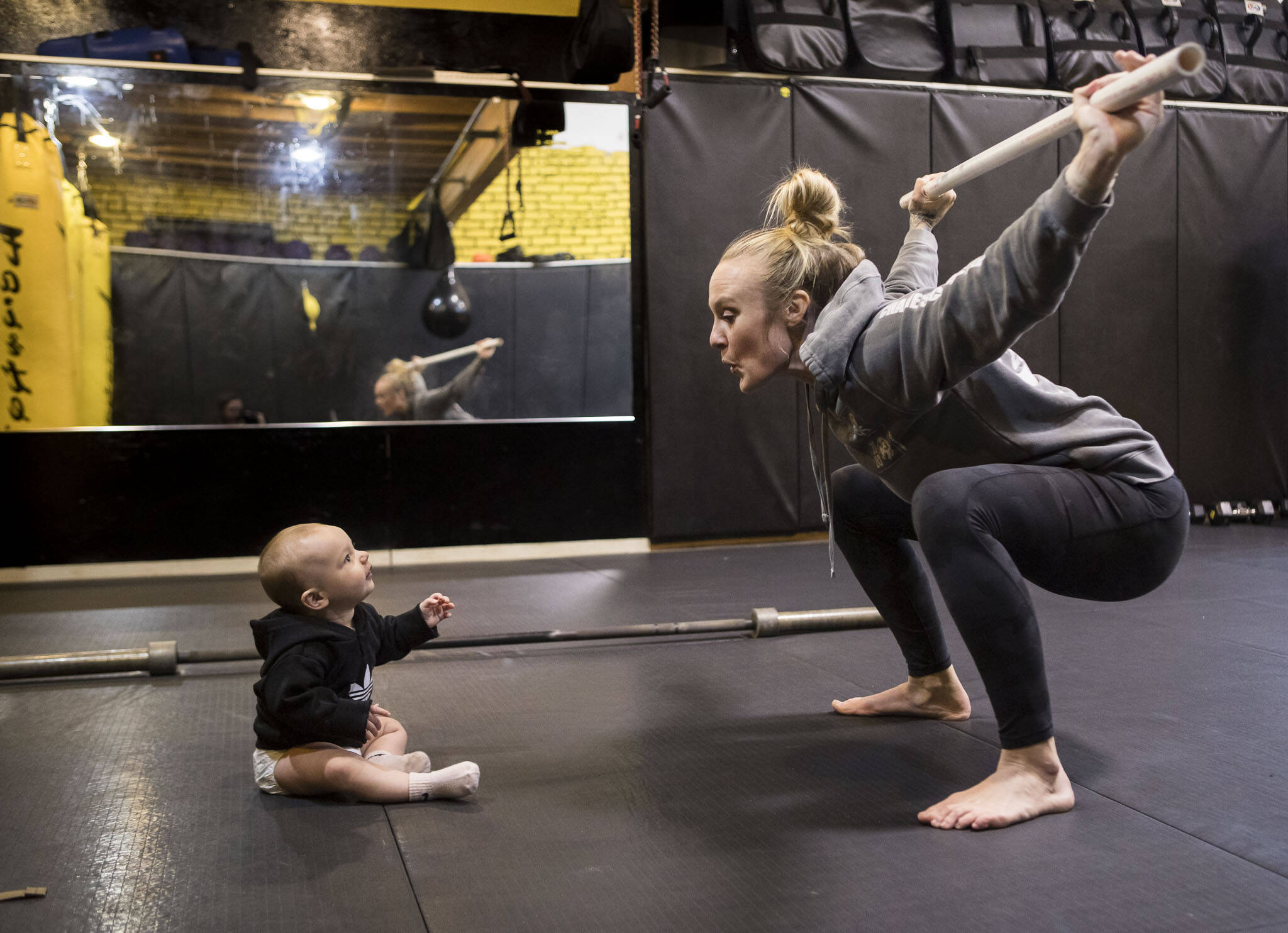 Miranda Granger makes a face at her daughter, Austin, while she does an overhead squat during a warmup in February 2022 at Charlie’s Combat Club in Everett, Washington. Six months after giving birth, Granger finally ramped up the intensity of her training. In the meantime, she had struggled with fatigue and pelvic floor issues. (Olivia Vanni / The Herald)