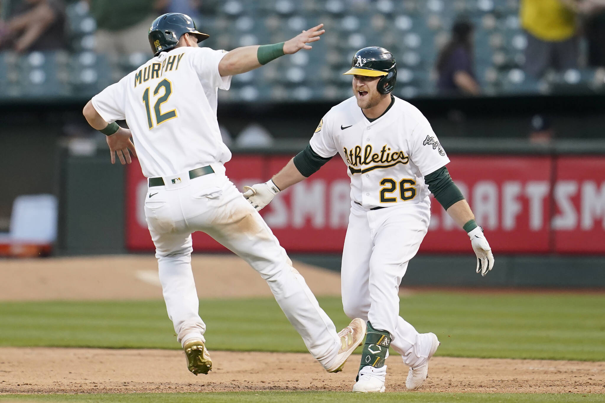 The Athletics’ Sheldon Neuse (26) is congratulated by Sean Murphy after hitting into a fielder’s choice that scored Tony Kemp with the winning run during the 10th inning of a game against the Mariners on Saturday in Oakland, Calif. (AP Photo/Jeff Chiu)
