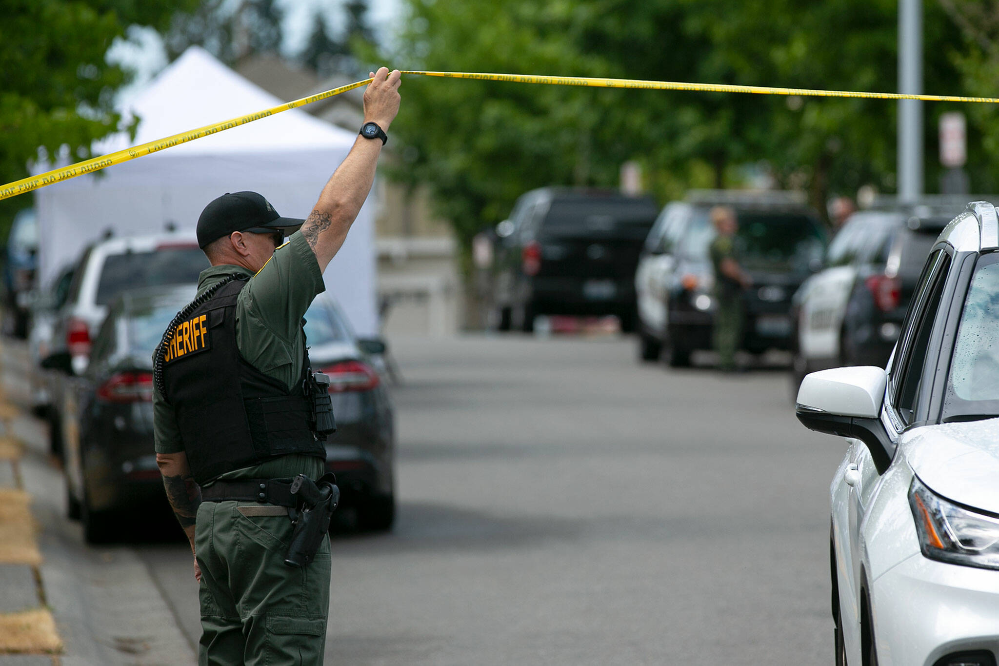 A sheriff’s deputy lets a vehicle pass police tape as law enforcement work on 96th Street SE where an overnight home invasion resulted in one person being killed on Friday, Aug. 19, in Everett. (Ryan Berry / The Herald)