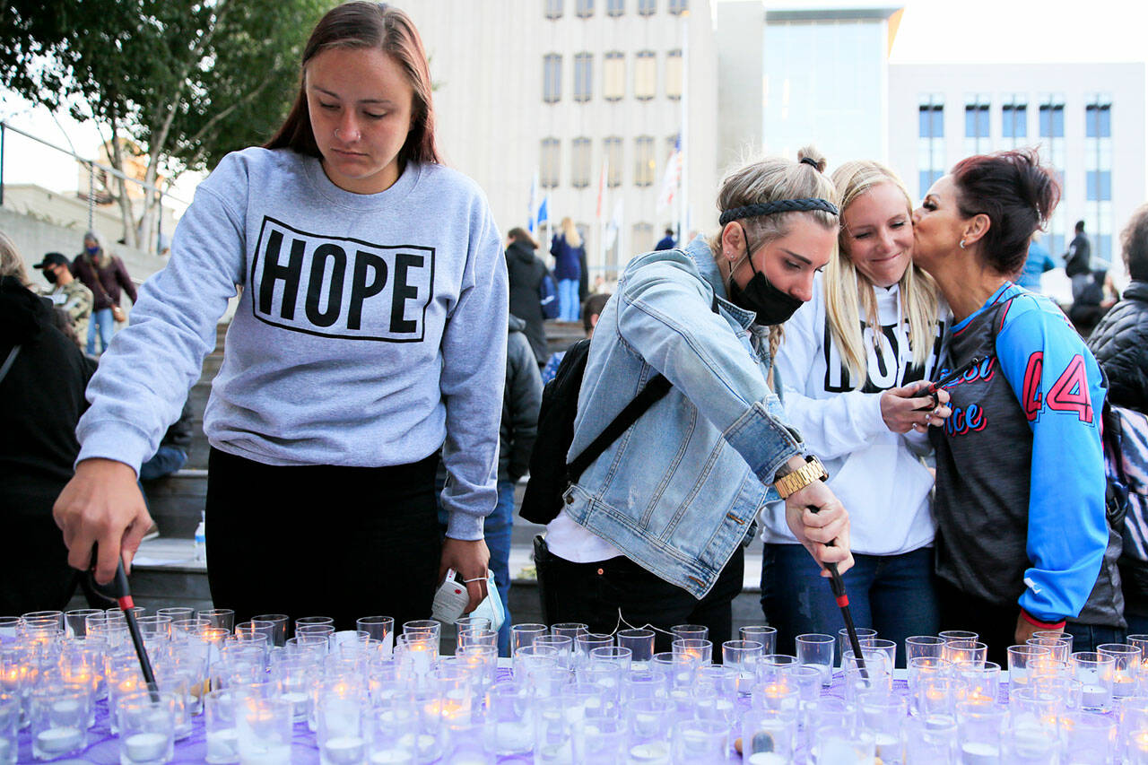 Gina Anderson (left) and Rae Dorcas light candles as Shana Morcom gets a kiss from Tamara Cooper at the Snohomish County Campus Plaza in Everett on August 31, 2021, during a vigil for the victims of drug overdoses. (Kevin Clark / The Herald file photo)