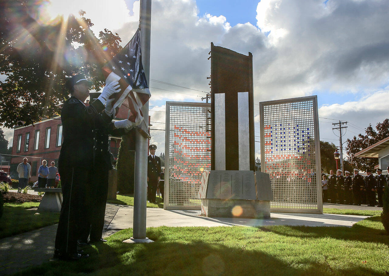Honor guard members, Steve Barnes, left, and Steven Francis, raises a flag to full extension and would lower it half staff at The Fallen Firefighter Memorial in Edmonds on Sept. 11, 2016. (Kevin Clark / The Herald)