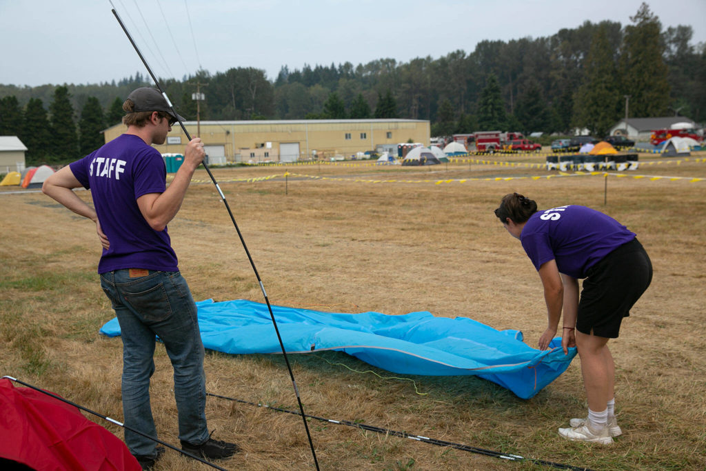 Brother and sister Forest and Sierra Meichtry set up a tent in preparation for staying overnight as they work for Bishop Services, who are providing mobile showers for firefighters camped at the fairgrounds on Sunday, Sep. 11, 2022, at the Evergreen State Fairgrounds in Monroe, Washington. (Ryan Berry / The Herald)
