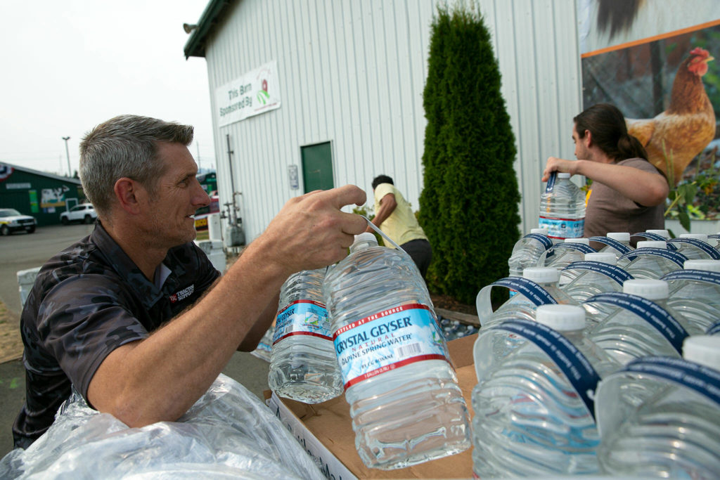 Phillip Spence, of Tractor Supply Co. in Monroe, unloads a pallet of water jugs donated by the company alongside Emilio Gomez and Michael Bilodeau on Sunday, Sep. 11, 2022, at the Evergreen State Fairgrounds in Monroe, Washington. (Ryan Berry / The Herald)