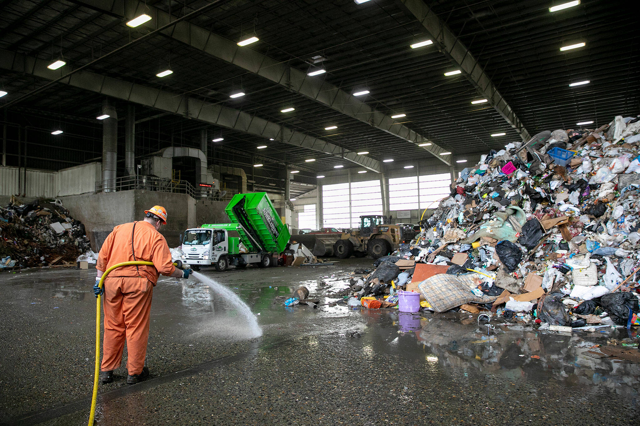 A worker is seen spraying down the floor of the Airport Road Recycling and Transfer Station during a period of backlogged garbage earlier this year on Friday, April 29, 2022, in Everett, Washington. (Ryan Berry / The Herald)