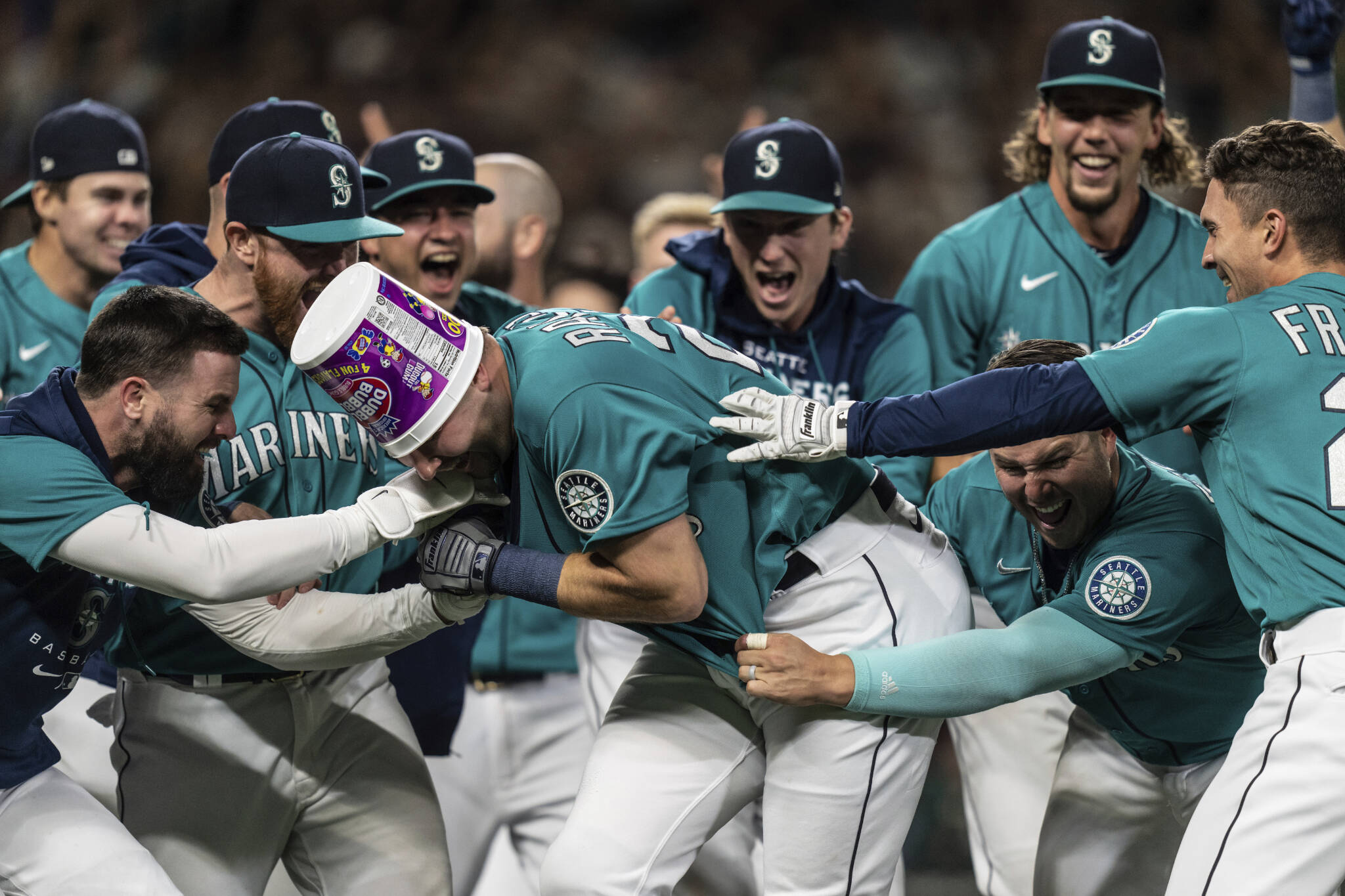 Mariners including Jesse Winker (left), Ty France (third from right), Logan Gilbert (second from right) and Adam Frazier (right) celebrate a walk-off home run by Cal Raleigh in ninth inning of a game against the Athletics on Friday in Seattle. The Mariners won 2-1 to clinch a spot in the playoffs. (AP Photo/Stephen Brashear)