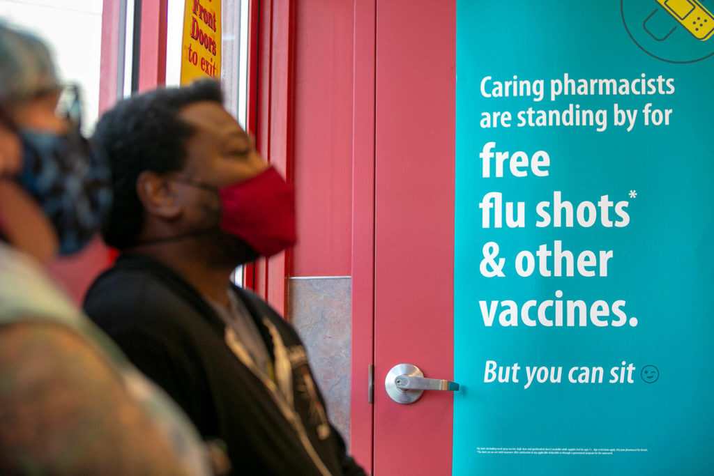 Sarah Sharkey and Shon Grimes wait Saturday to get their COVID booster shots at Bartell Drugs on Broadway in Everett. (Ryan Berry / The Herald)
