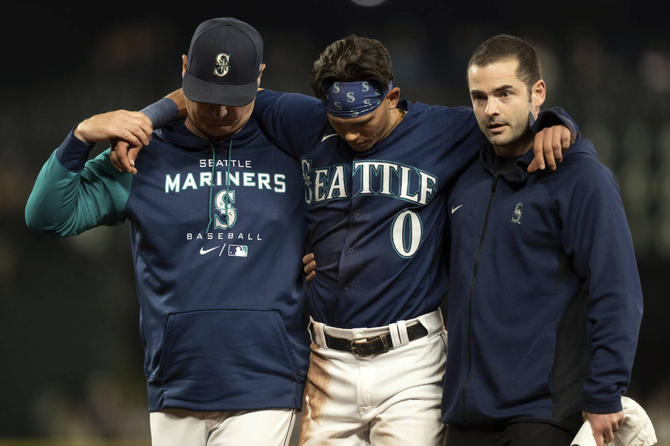 Seattle Mariners' Sam Haggerty, center, is helped off the field by training personnel manager Scott Servais, left, while stealing second base during the ninth inning of a baseball game against the Detroit Tigers, Monday, Oct. 3, 2022, in Seattle. The Tigers won 4-3. (AP Photo/Stephen Brashear)