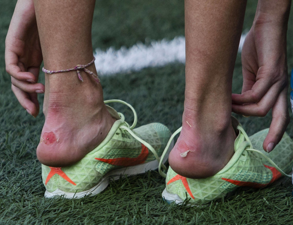 A runner pulls off their spiked shoes to relieve blisters on the back of their heels at the Hole In The Wall Invitational on Saturday, Oct. 8, 2022 in Arlington, Washington. (Olivia Vanni / The Herald)
