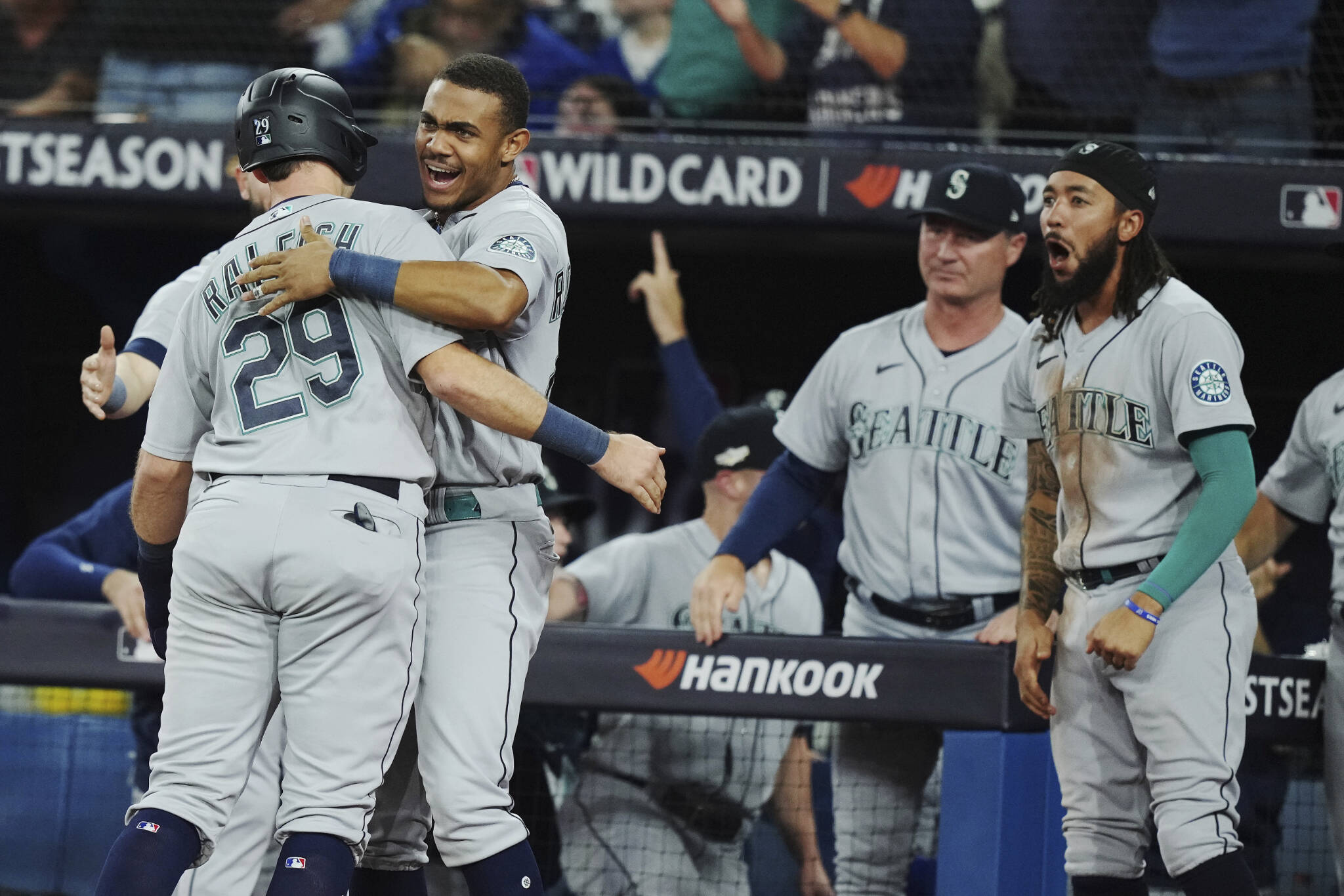 The Mariners Cal Raleigh (29) celebrates with Julio Rodriguez after scoring on a double by Adam Frazier, as J.P. Crawford (right) reacts during the ninth inning of Game 2 of an AL wild-card playoff series against the Blue Jays on Saturday in Toronto. (Nathan Denette/The Canadian Press via AP)