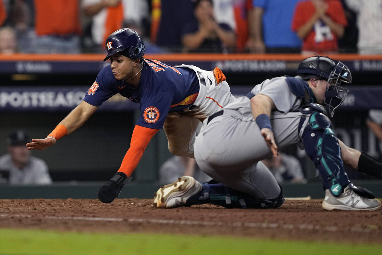 Houston Astros' Jeremy Pena, left, scores past Seattle Mariners catcher Cal Raleigh, right, during the eighth inning on a hit by teammate Alex Bregman in Game 2 of an American League Division Series baseball game in Houston, Thursday, Oct. 13, 2022. (AP Photo/David J. Phillip)