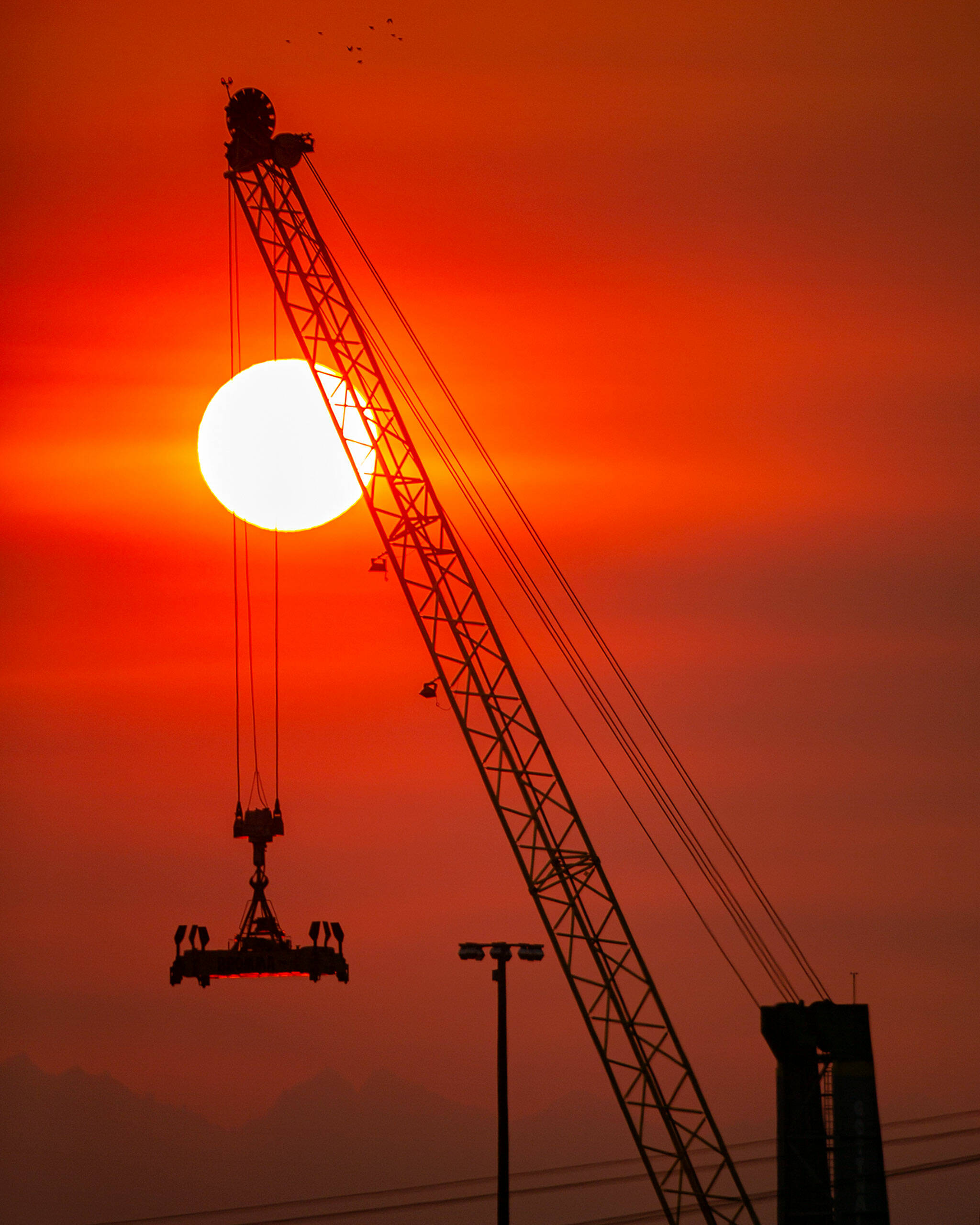 The sun turns a deep red as it sets beyond the Port of Everett and the Olympic Mountains on a hazardously smoky evening Sunday, in Everett. (Ryan Berry / The Herald)