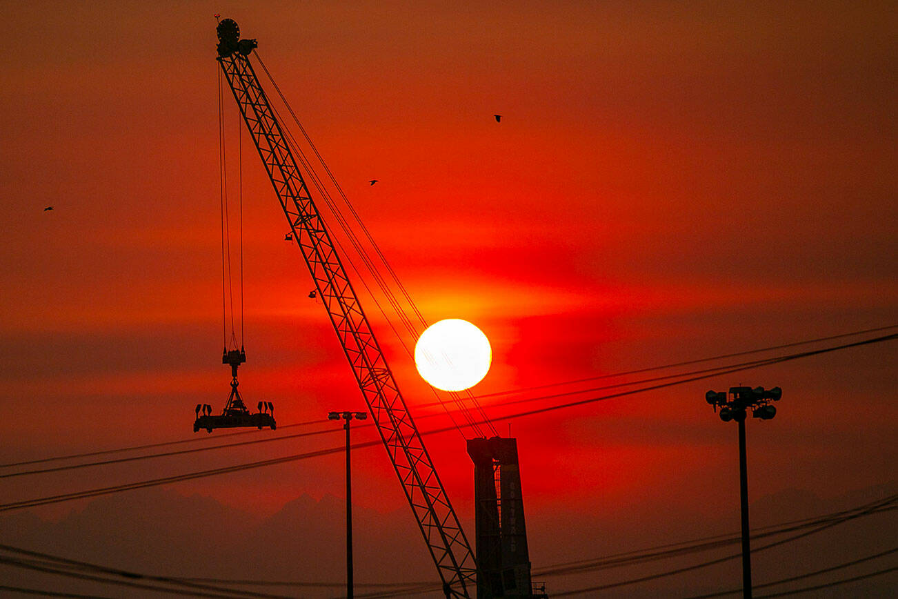 The sun turns a deep red as it sets beyond the Port of Everett and the Olympic Mountains on a hazardously smoky evening Sunday, Oct. 16, 2022, in Everett, Washington. (Ryan Berry / The Herald)