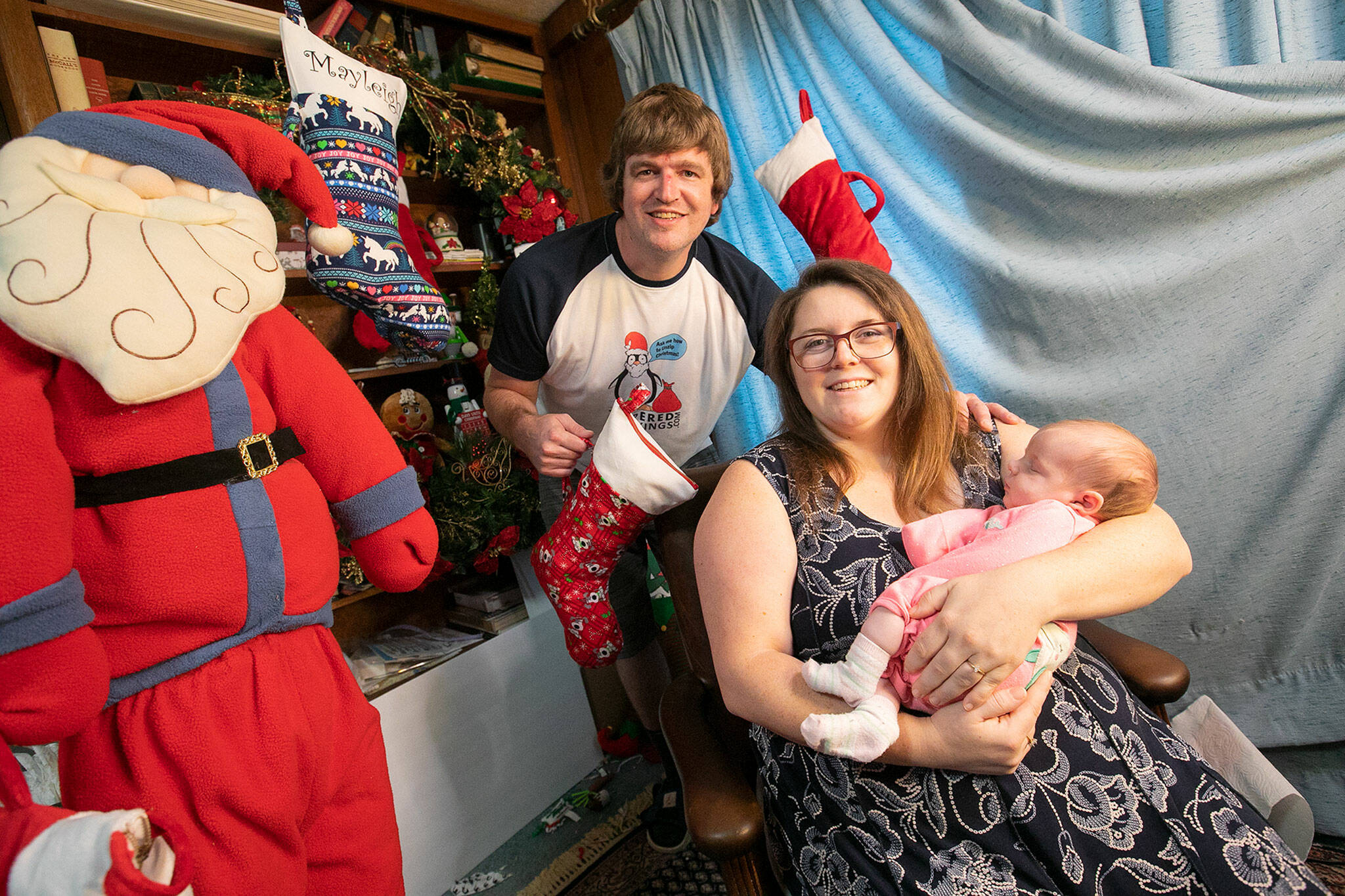 Alex Phillips, Karen Mahood and their 4-week-old baby Georgia sit inside the family’s Mukilteo where the production and television sales of Zippered Stockings take place. (Ryan Berry / The Herald)