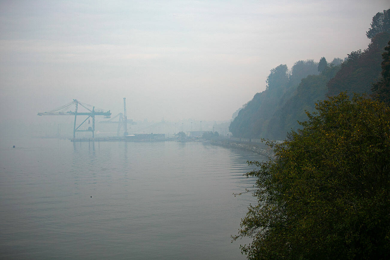Cranes at the Port of Everett, which normally make up a larger skyline, are barely visible from the staircase at Howarth Park on Thursday, Oct. 20, 2022, in Everett, Washington. Wildfire smoke has been choking the region, but forecasts calling for rain mean the haze may finally clear in the coming days. (Ryan Berry / The Herald)