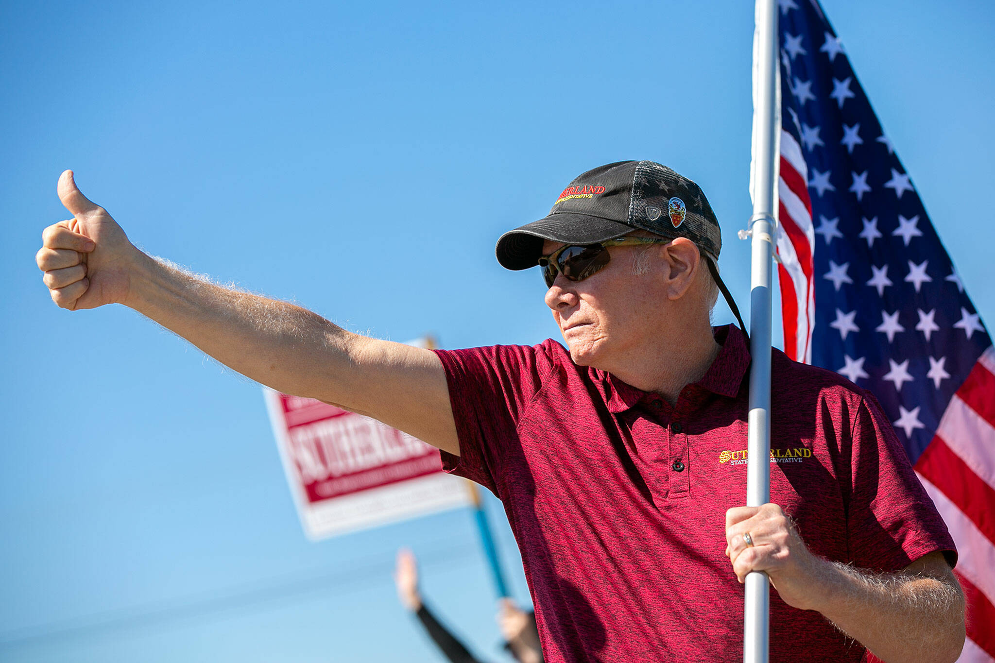 State Representative Robert Sutherland gives a thumbs-up to passing drivers as he and a few volunteers wave flags and campaign signs along the side of State Route 9 on July 22, in Lake Stevens. (Ryan Berry / The Herald)