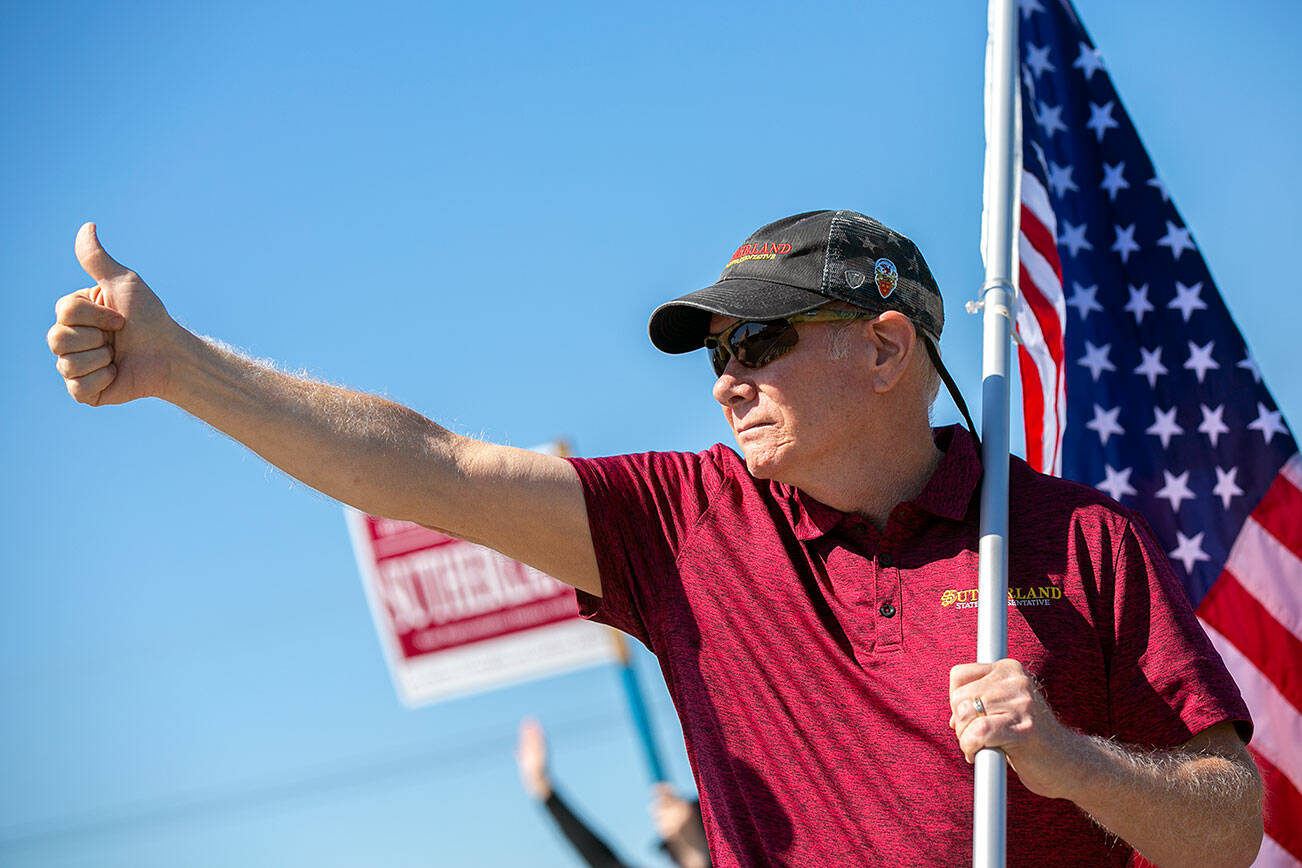 State Representative Robert Sutherland, who is seeking re-election in the 39th District this year, gives a thumbs-up to passing drivers as he and a few volunteers wave flags and campaign signs along the side of State Route 9 on Friday, July 22, 2022, in Lake Stevens, Washington. (Ryan Berry / The Herald)