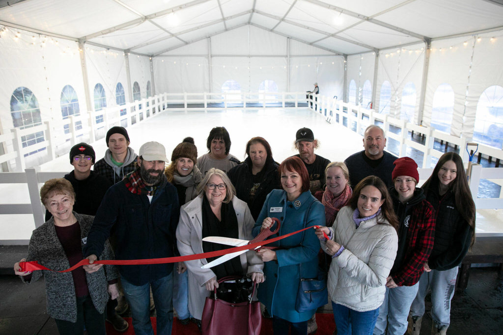 Local leaders and workers at Blue Line Sports and Entertainment gather to cut the ribbon on Arlington’s new seasonal ice rink Friday at Legion Memorial Park. (Ryan Berry / The Herald) 

