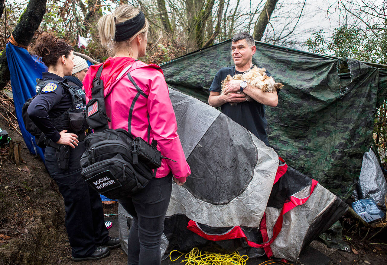 An Everett police officer and a social worker (foreground) chat with Chris Portner (right) and his dog Gizzy at a homeless encampment near I-5 and Marine View Drive during the annual Point in Time count Jan. 23, 2019, in Everett. (Olivia Vanni / Herald file)