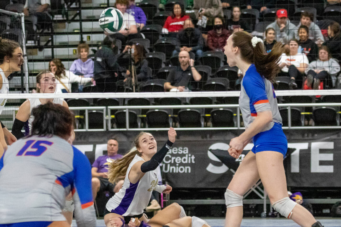 Lake Stevens' Katelyn Eichert (24) reaches over teammate Alyss Kelly to punch the ball up as Graham-Kapowsin celebrates another point during the WIAA state volleyball championship on Saturday, Nov. 19, 2022, at the Yakima Valley SunDome in Yakima, Wash. Graham-Kapowsin defeated Lake Stevens 3-0 to win the state championship 25-21, 25-18 and 25-22. (TJ Mullinax/for The Herald)