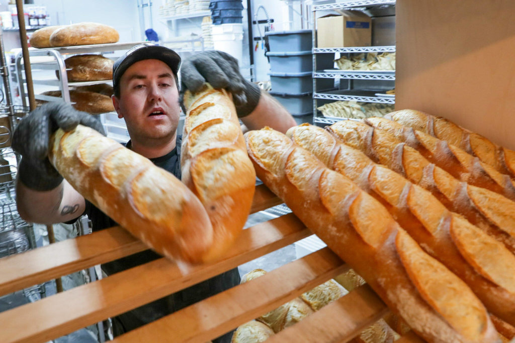 Conor O’Neill racks freshly baked baguettes Friday morning at The Cottage Community Bakery on Sept. 30, in Edmonds. (Kevin Clark / The Herald)
