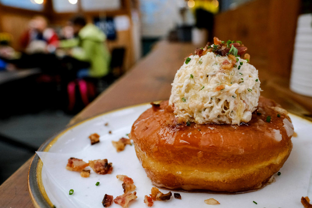 The crab doughnut at Market in Edmonds is a strange delight, with a sweet and dense glazed doughnut topped with bright and briny dungeness crab salad, nutty browned butter and a shower of smoky bacon bits. (Taylor Goebel / The Herald)
