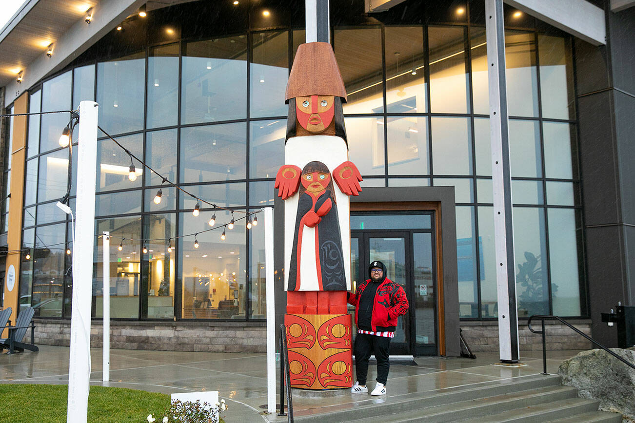 Ty Juvinel stands beside the towering welcome figure that he created for the Edmonds Waterfront Center on Friday, Nov. 25, 2022, in Edmonds, Washington. (Ryan Berry / The Herald)