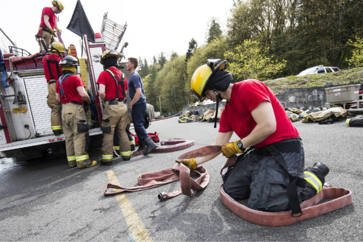 After a day of learning to fight fires, Snohomish firefighter recruit Chau Nguyen flakes a hose as other recruits load the hoses onto a fire truck April 19, 2018, at the training facility on S. Machias Rd. in Snohomish. (Andy Bronson / Herald file)
