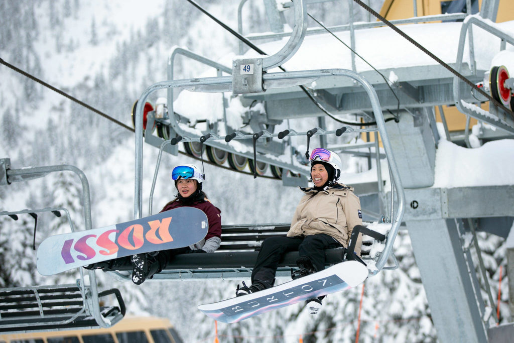 Two snowboarders head up the mountain in a lift chair. (Ryan Berry / The Herald)
