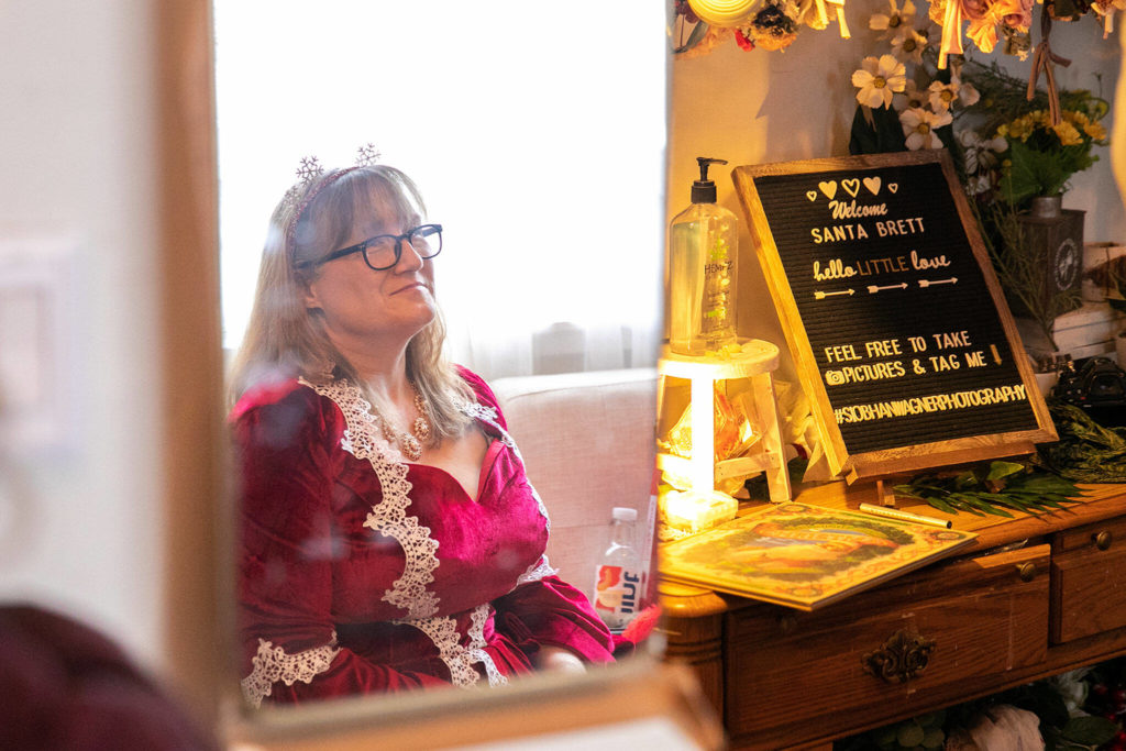 Tami Nichols, wearing her Mrs. Claus wedding dress, watches as her husband Brett Nichols takes Christmas photos with a family on Dec. 4, in Monroe. (Ryan Berry / The Herald)
