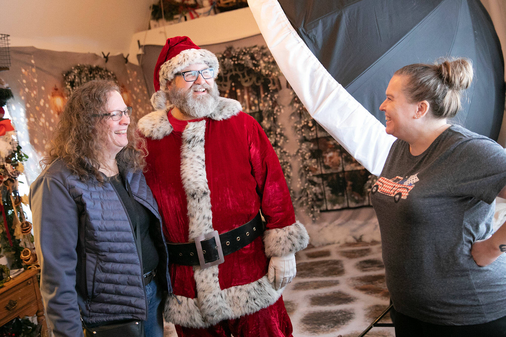 Santa Brett Nichols chats with Kristin Johnson, left, and photographer Stacy Yonkaitis, after doing a photo shoot with the Johnson family on Dec. 4, in Monroe. The three go back to their days at Sultan High School roughly 30 years ago, and have been doing yearly Christmas photos together for almost a decade. (Ryan Berry / The Herald)
