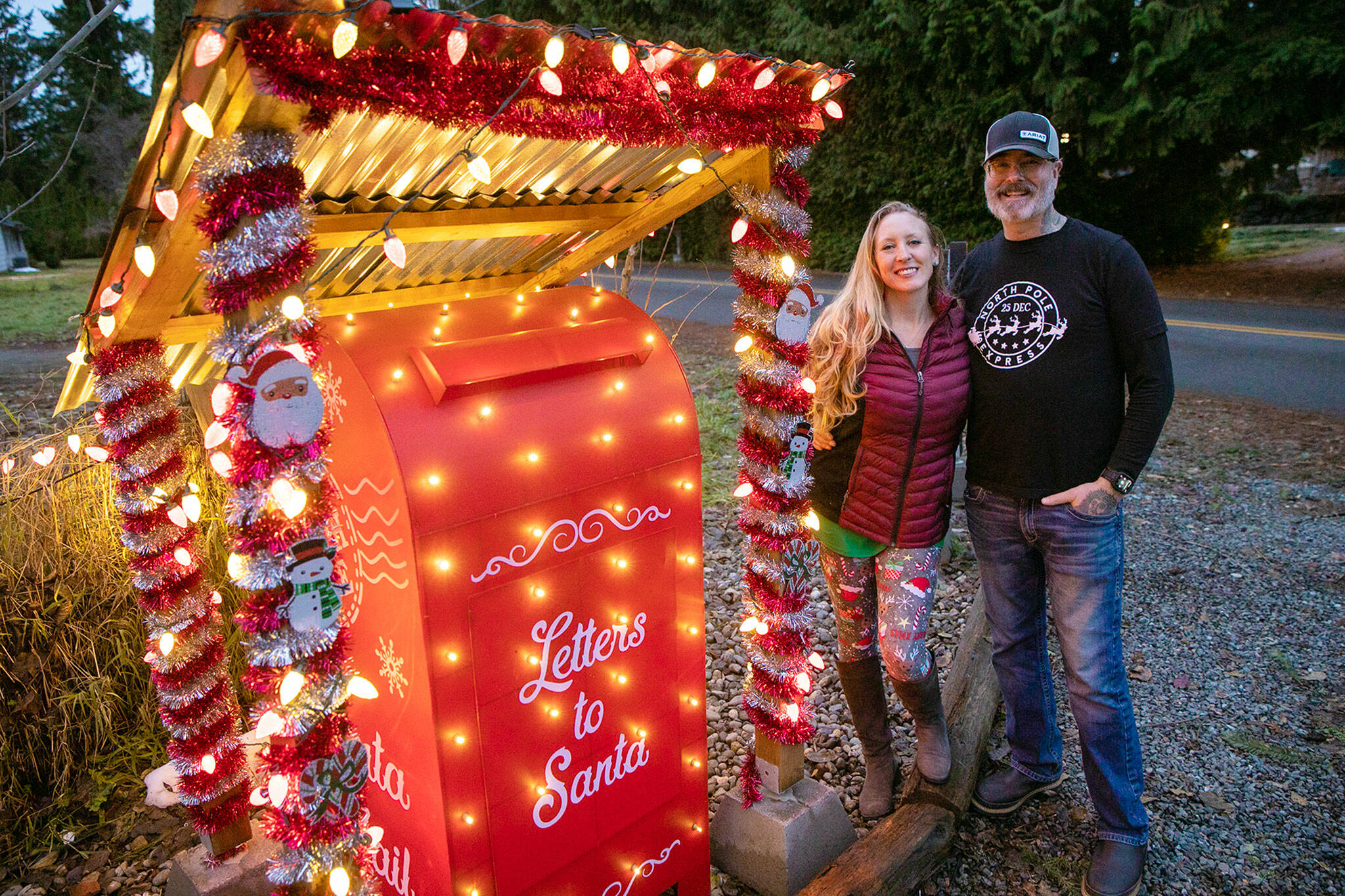Lena and Brian Schultz stand in front of their home next to their mailbox for Letters to Santa at Living Aloha Farm in Lake Stevens. The couple have been receiving and responding to letters destined for the North Pole since 2019. (Ryan Berry / The Herald)