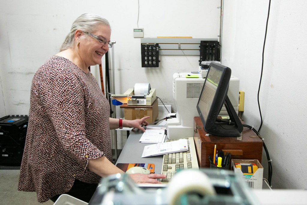 Barbara Reed feeds film through a scanner while working in the lab at Ken’s Camera on Thursday, Dec. 15, 2022, in Everett, Washington. “I’m going to miss traveling through other people’s photos,” Reed said, adding she had seen just about every destination the world has to offer through her work processing film. (Ryan Berry / The Herald)
