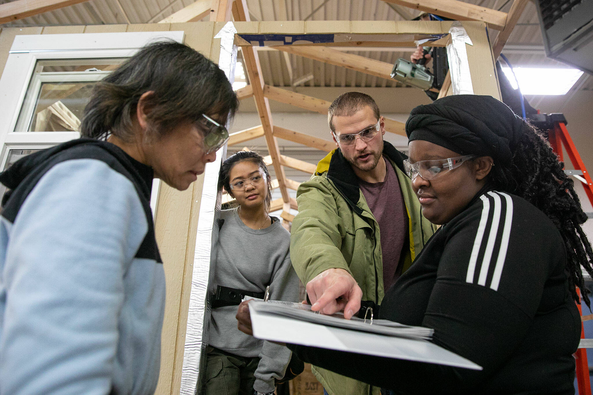 Brad Farnum, third from left, facilitator 2 at Edmonds College, goes over blueprints with students, from left, Lisa Doan, Angelica Subillaga and Regina Lewis while they work on constructing a tiny home with classmates in their Advanced Manufacturing Skills Center Construction Pre-Apprenticeship Program class on Monday, Dec. 12, 2022, at the Washington Aerospace Training & Research Center in Everett, Washington. (Ryan Berry / The Herald)