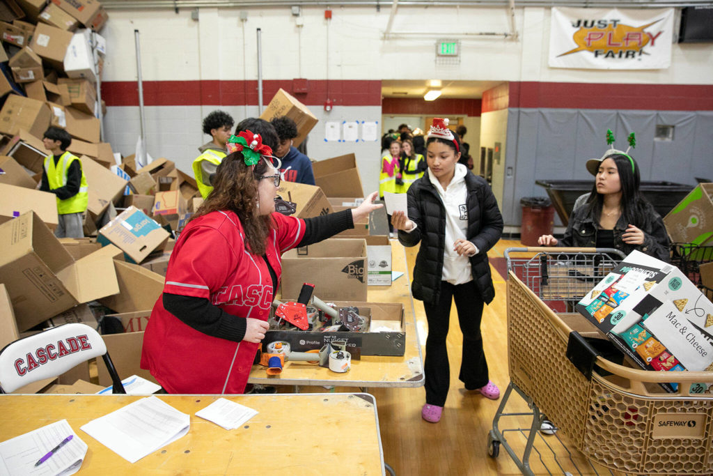 Bethany Rickard, an AP U.S. history and AP human geography teacher at Cascade, helps keep the line moving as volunteers fill boxes with food during Cascade’s annual holiday food drive Wednesday, Dec. 14, at Cascade High School in Everett. (Ryan Berry / The Herald)

