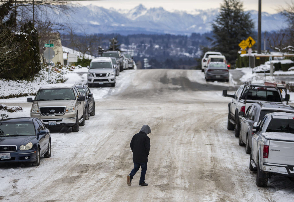 A pedestrian navigates compact snow and ice while crossing the street on Thursday, in Everett. (Olivia Vanni / The Herald)
