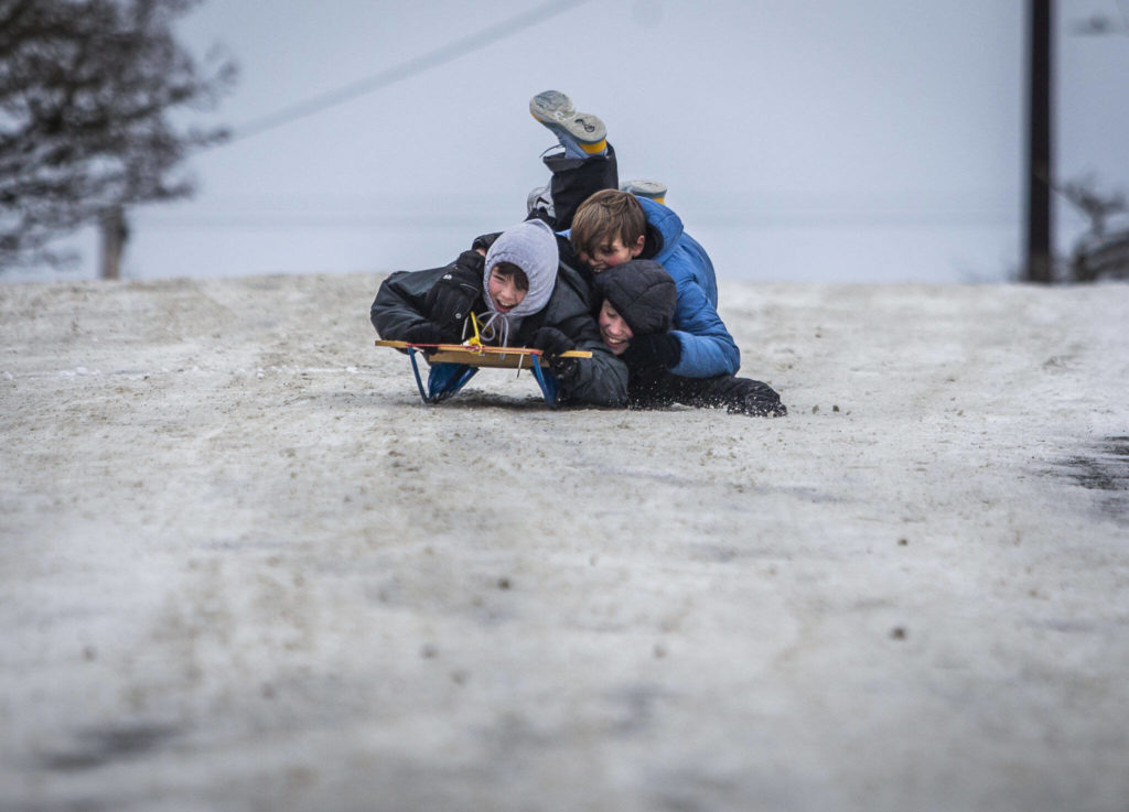 Ray Hendry, Corbyn Scervik and Same Lane try to all fit on one sled as they navigate their way down the hill on Thursday, in Everett. (Olivia Vanni / The Herald)
