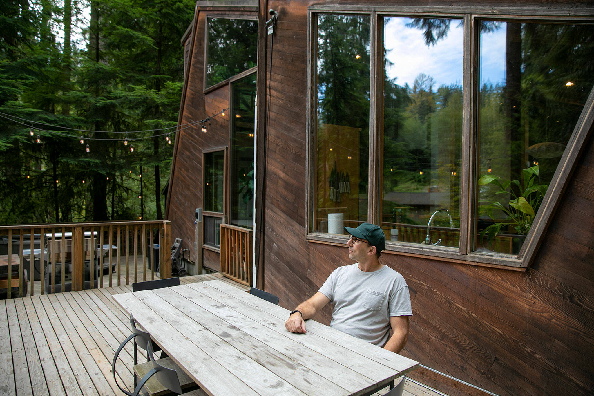 Canyon Creek Cabins co-owner Andy Whitcomb relaxes on the deck behind Cabin 1, an upgraded 1970s A-frame. (Ryan Berry / The Herald)